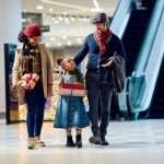A happy family walks through a mall with their daughter, smiling as they shop for Christmas presents.