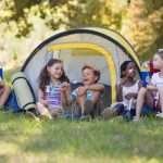 A group of happy campers eat marshmallows at camp during summer break.